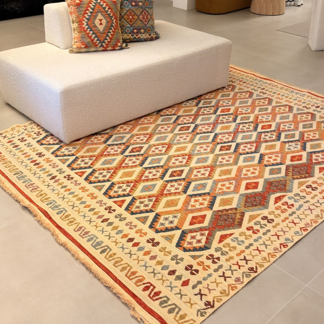 Tapete kilim Ravena 1001, com losangos em faixas em terracota, azul e ocre sobre fundo cru, e franjas nas pontas